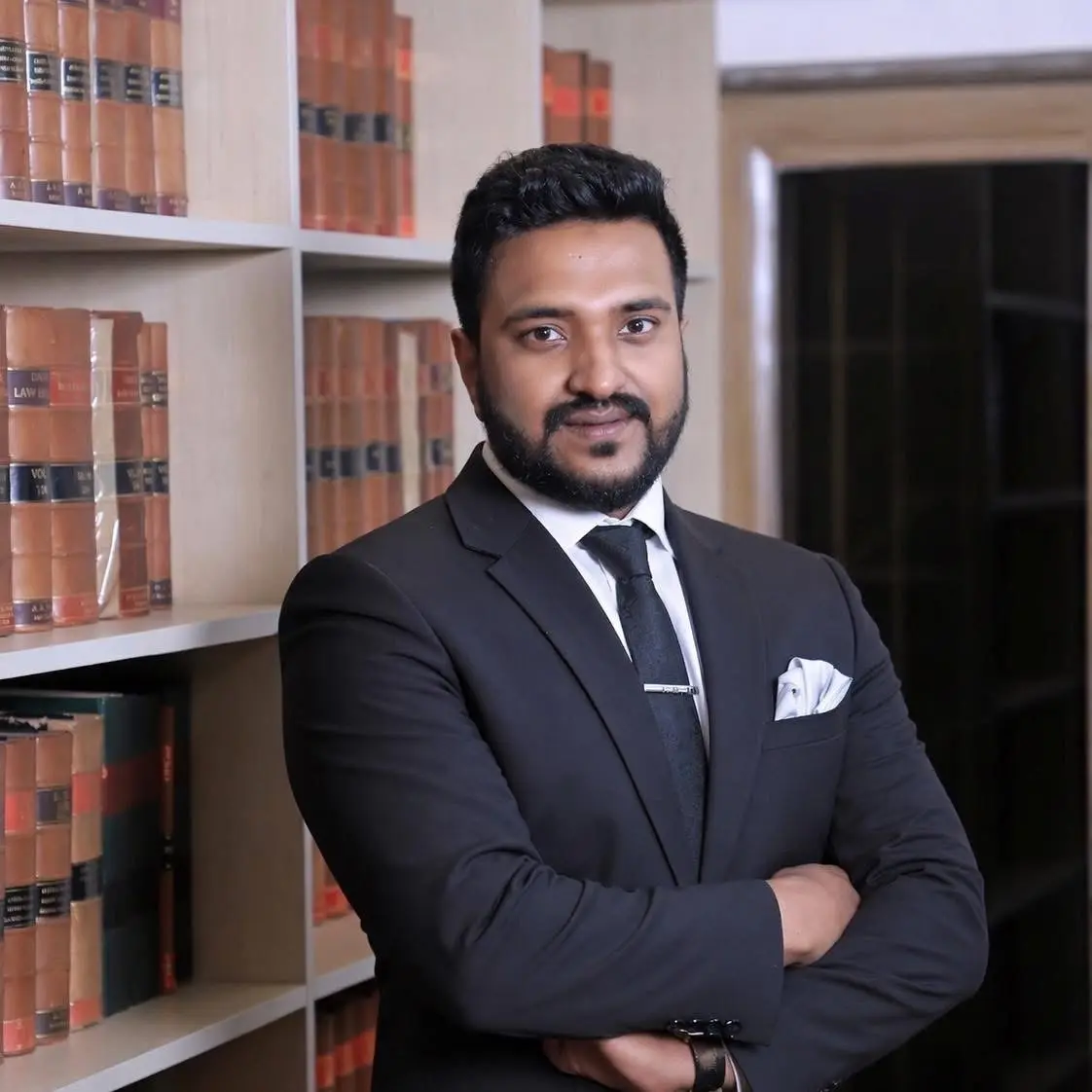 Cyrus Anushirvan Faizi in a black suit beside a bookcase